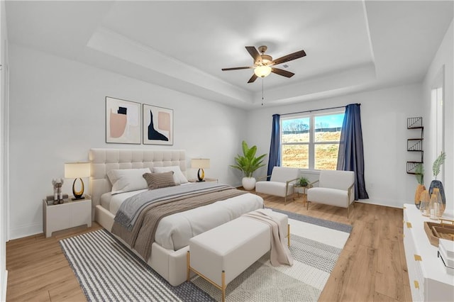 bedroom featuring light wood-type flooring, ceiling fan, and a tray ceiling