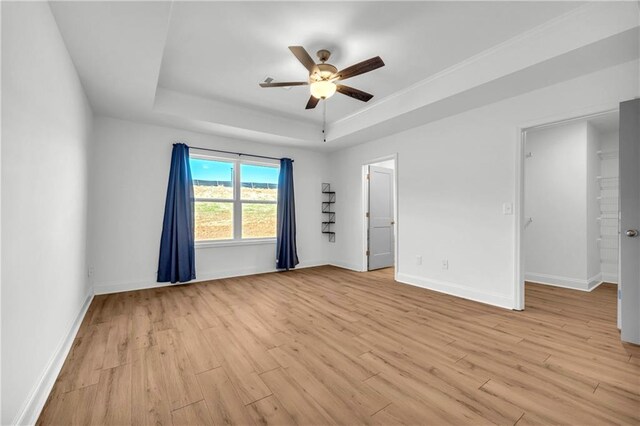 empty room featuring light wood-type flooring, ceiling fan, and a raised ceiling