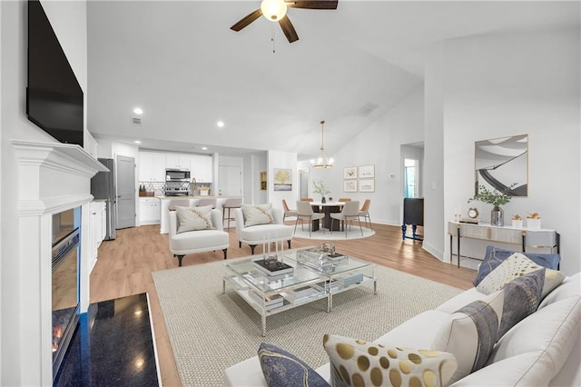 living room with lofted ceiling, light wood-type flooring, and ceiling fan with notable chandelier