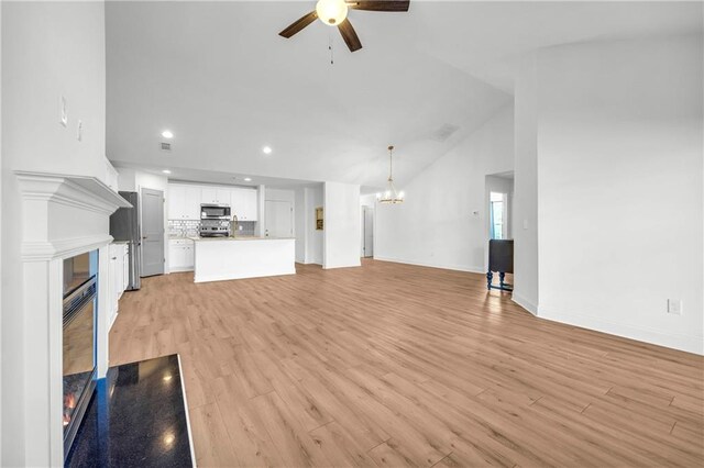 unfurnished living room with ceiling fan with notable chandelier, lofted ceiling, and light wood-type flooring