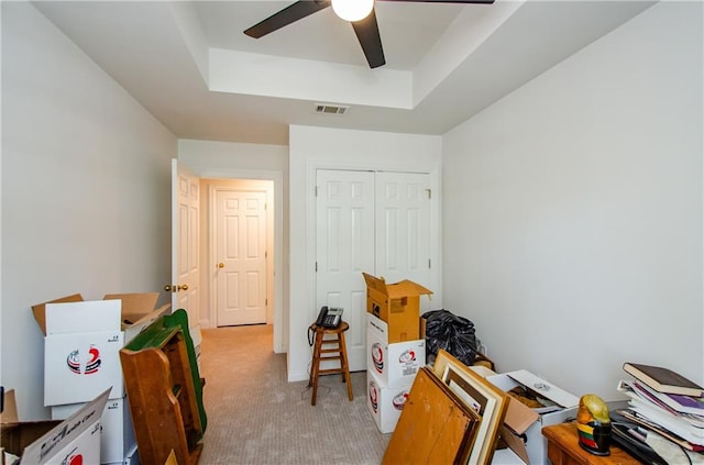 office space with a tray ceiling, light carpet, and ceiling fan