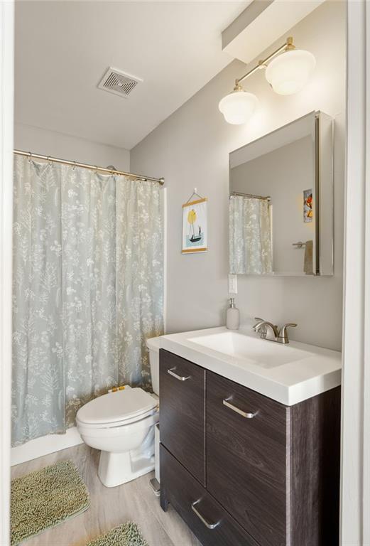 full bath featuring toilet, wood finished floors, vanity, visible vents, and a shower with curtain