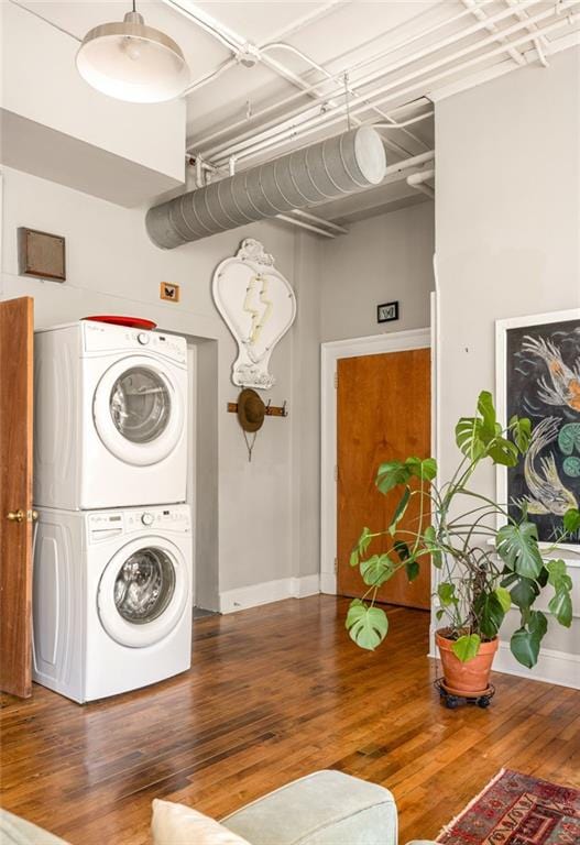 washroom with stacked washing maching and dryer, baseboards, laundry area, and wood finished floors