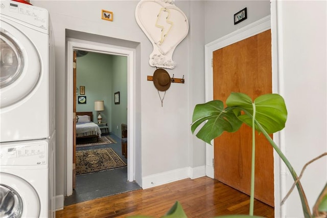 clothes washing area featuring stacked washer / dryer, baseboards, and wood finished floors