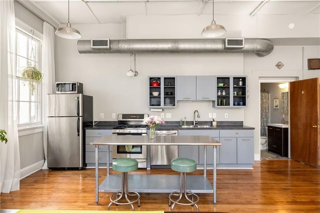 kitchen featuring stainless steel appliances, a sink, visible vents, open shelves, and dark countertops