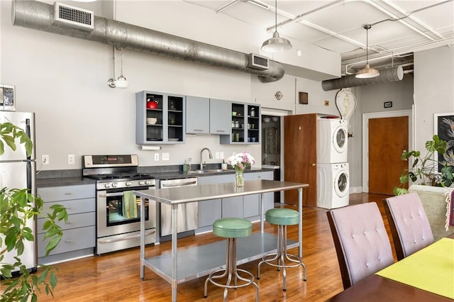 kitchen featuring visible vents, dark countertops, appliances with stainless steel finishes, stacked washer / drying machine, and a sink