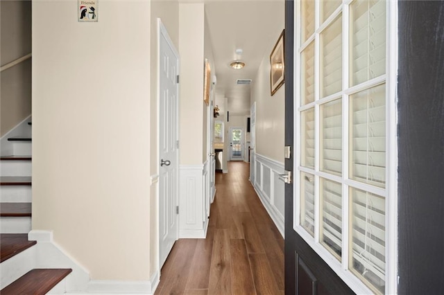 corridor featuring dark wood-style floors, a wainscoted wall, and a decorative wall