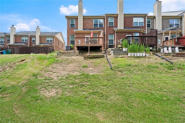 rear view of property featuring brick siding, a wooden deck, a chimney, a lawn, and a residential view