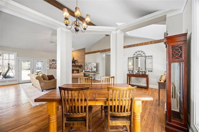 dining area featuring a fireplace, wood-type flooring, vaulted ceiling with beams, an inviting chandelier, and french doors