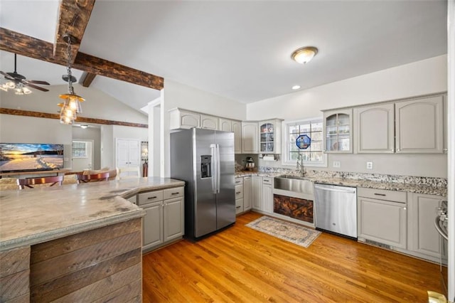 kitchen featuring appliances with stainless steel finishes, vaulted ceiling with beams, gray cabinetry, sink, and light wood-type flooring