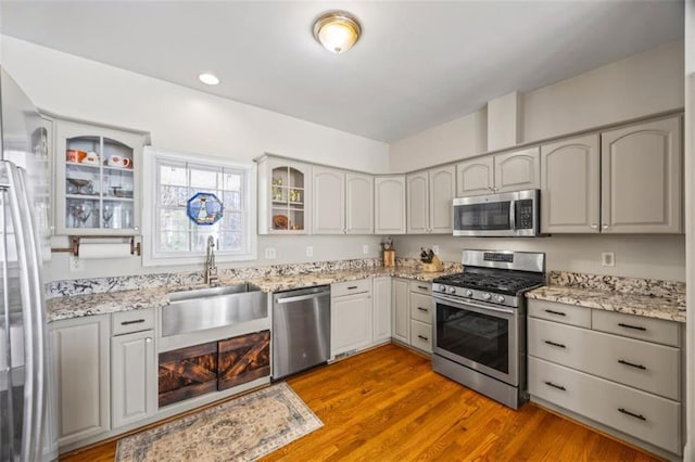 kitchen featuring gray cabinets, appliances with stainless steel finishes, sink, light stone counters, and light hardwood / wood-style floors