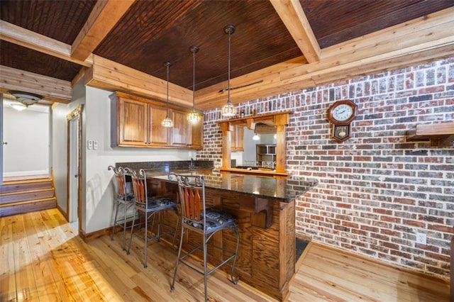 kitchen featuring pendant lighting, light hardwood / wood-style flooring, dark stone countertops, a kitchen bar, and brick wall