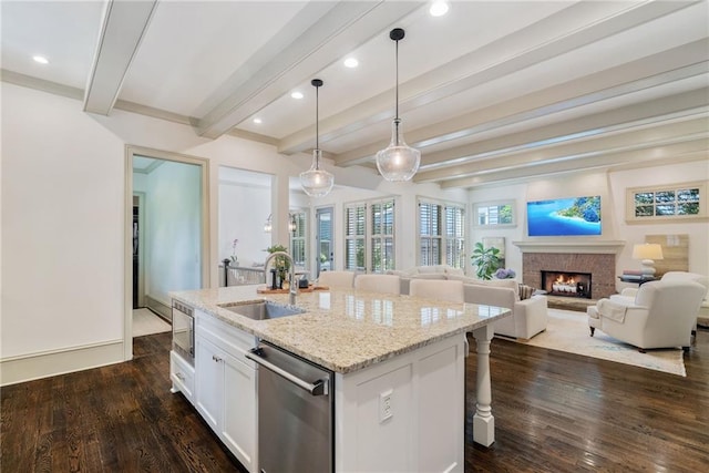 175 Centennial Trce, Roswell, GA 30076 - kitchen featuring appliances with stainless steel finishes, a warm lit fireplace, beamed ceiling, an island with sink, and white cabinetry