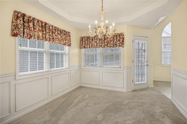 unfurnished dining area featuring a raised ceiling, wainscoting, an inviting chandelier, carpet flooring, and a decorative wall