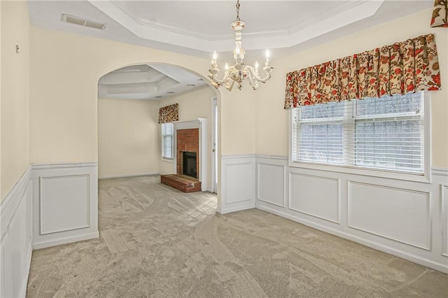 unfurnished dining area with arched walkways, a raised ceiling, light colored carpet, visible vents, and a brick fireplace