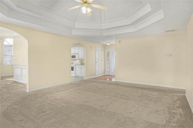 empty room featuring arched walkways, a tray ceiling, and ornamental molding