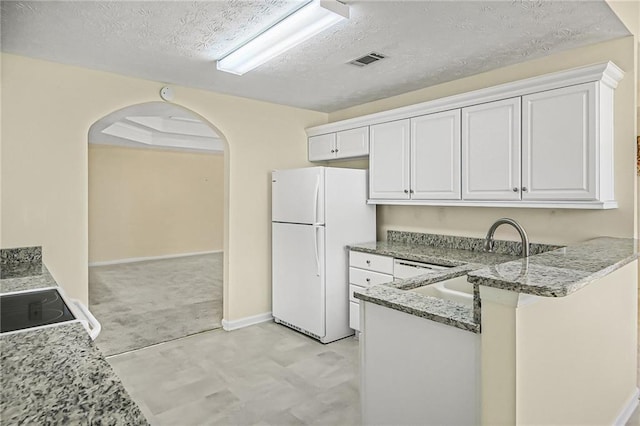 kitchen featuring visible vents, arched walkways, freestanding refrigerator, light stone countertops, and a sink