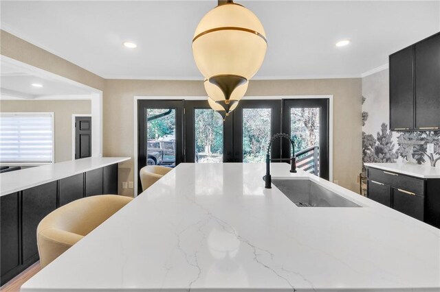 kitchen featuring light stone counters, sink, an island with sink, and hanging light fixtures