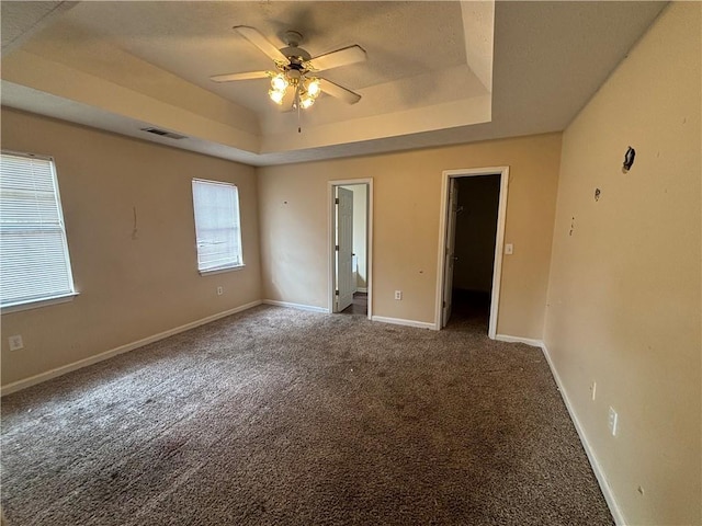 empty room with ceiling fan, carpet flooring, and a tray ceiling