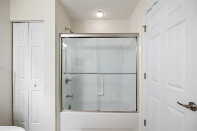 bathroom featuring toilet, combined bath / shower with glass door, and a textured ceiling