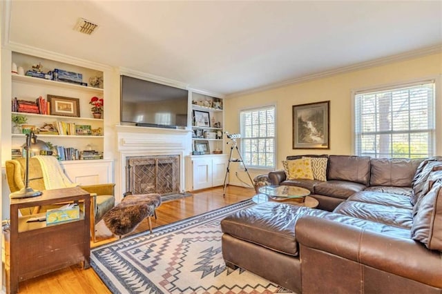 living room with ornamental molding, built in features, and light wood-type flooring