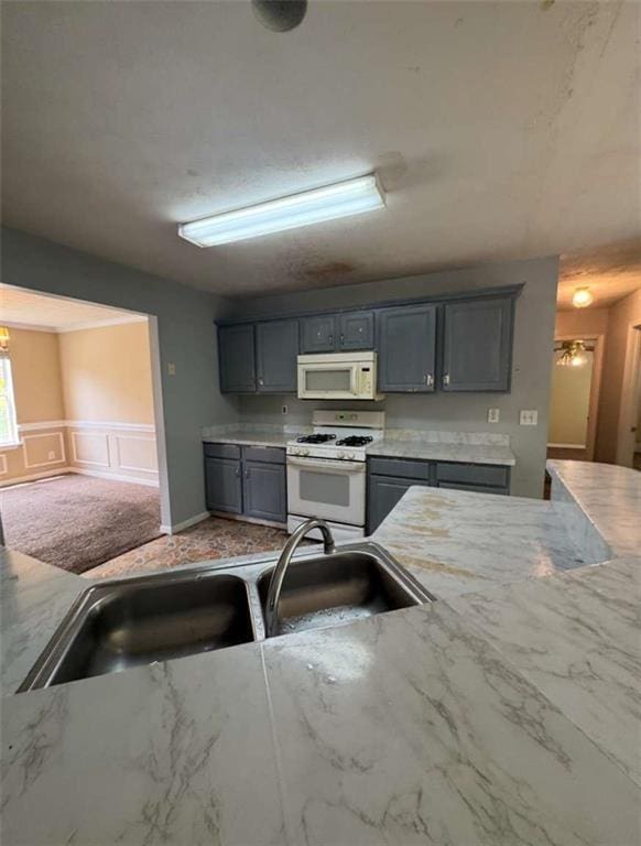 kitchen featuring white appliances, gray cabinetry, a sink, a decorative wall, and light stone counters