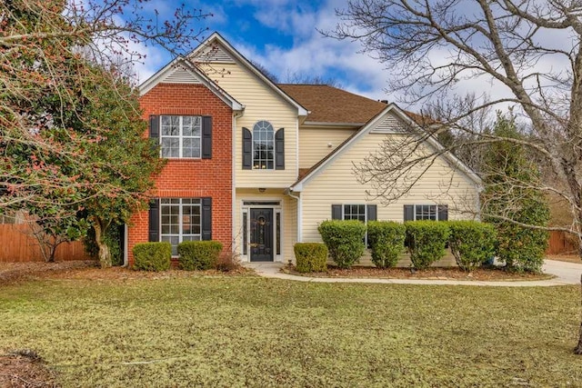 traditional-style home featuring a front lawn, fence, and brick siding