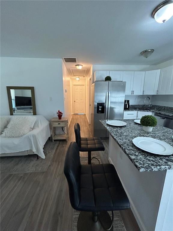 kitchen featuring dark wood-style flooring, visible vents, appliances with stainless steel finishes, white cabinets, and dark stone counters