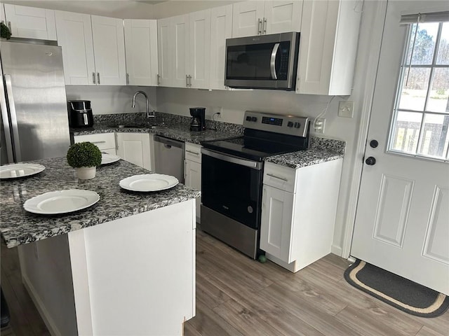 kitchen featuring light wood finished floors, appliances with stainless steel finishes, white cabinetry, a sink, and dark stone counters