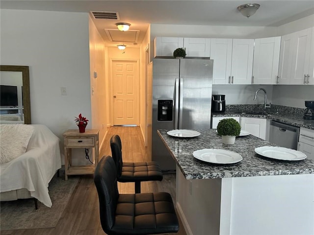 kitchen featuring wood finished floors, a sink, visible vents, white cabinetry, and appliances with stainless steel finishes