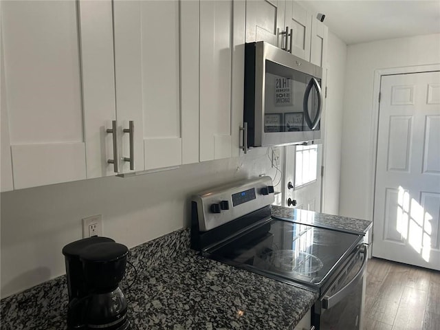 kitchen featuring stainless steel appliances, dark stone countertops, light wood finished floors, and white cabinetry