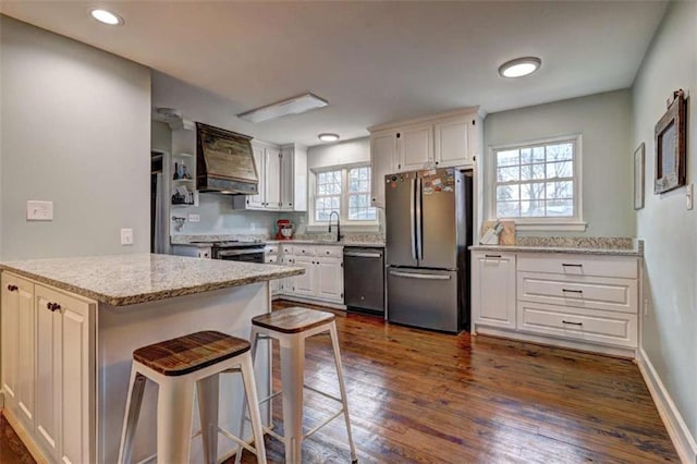 kitchen featuring a breakfast bar, custom exhaust hood, white cabinetry, stainless steel appliances, and light stone countertops