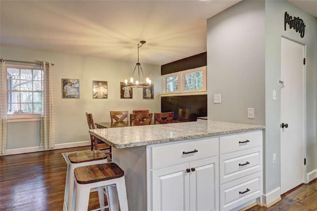 kitchen featuring dark hardwood / wood-style floors, a breakfast bar, pendant lighting, white cabinetry, and light stone counters