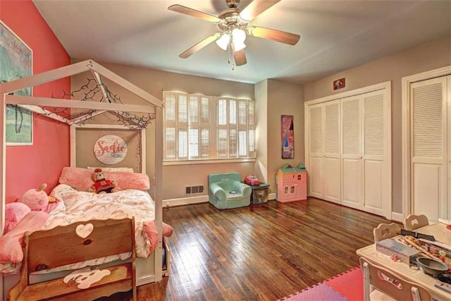 bedroom with dark wood-type flooring, ceiling fan, and two closets