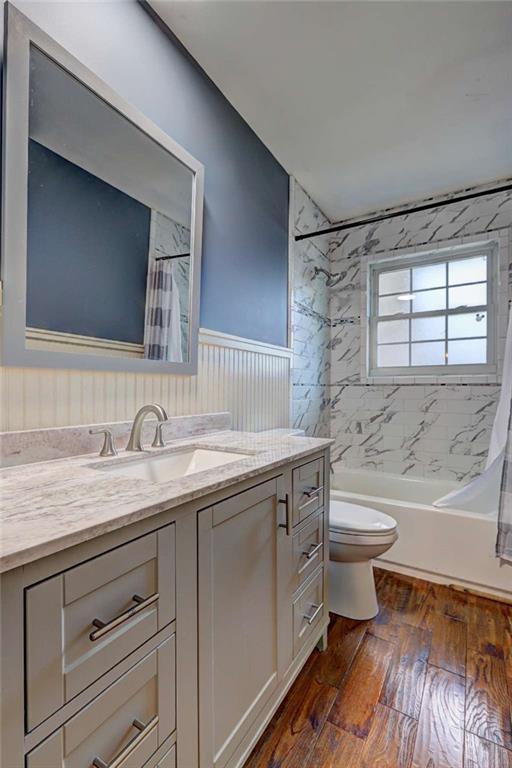 full bathroom with hardwood / wood-style flooring, vanity, shower / tub combo, and toilet