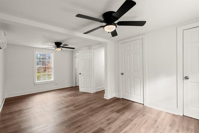 unfurnished bedroom featuring ceiling fan, wood-type flooring, and an AC wall unit