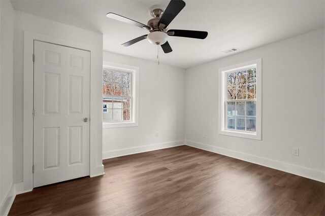 unfurnished room featuring ceiling fan, a healthy amount of sunlight, and dark wood-type flooring