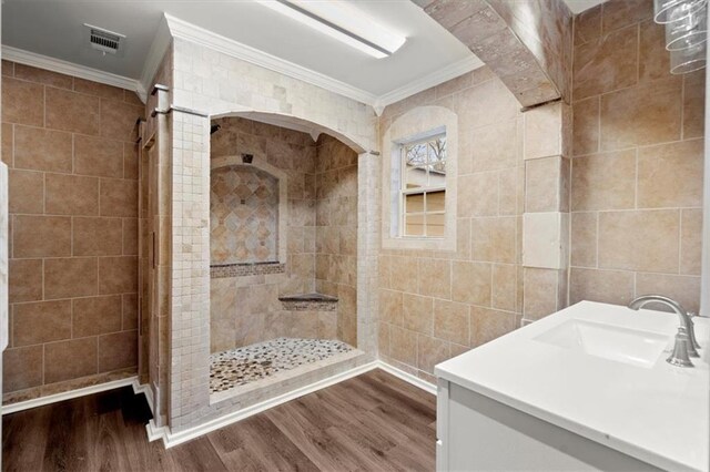 bathroom featuring a tile shower, wood-type flooring, tile walls, and ornamental molding