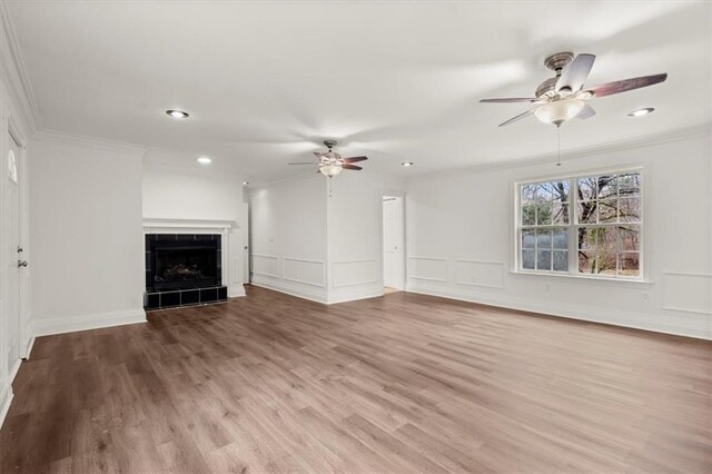 unfurnished living room with a tiled fireplace, crown molding, and light wood-type flooring