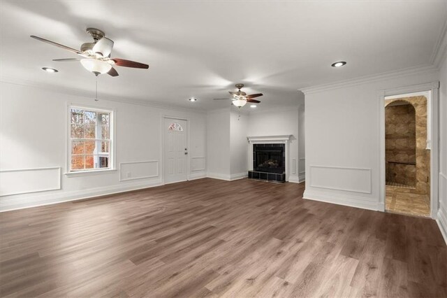 unfurnished living room featuring ceiling fan, wood-type flooring, ornamental molding, and a tiled fireplace