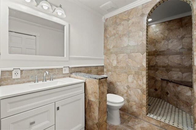 bathroom featuring ornamental molding, vanity, tiled shower, tile walls, and toilet