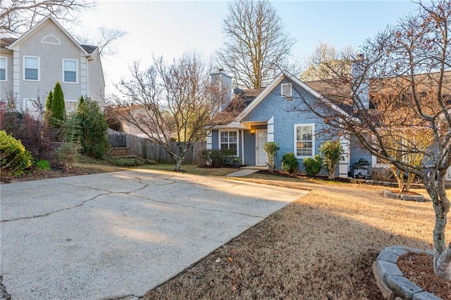 view of front of home featuring stucco siding, driveway, a chimney, and fence