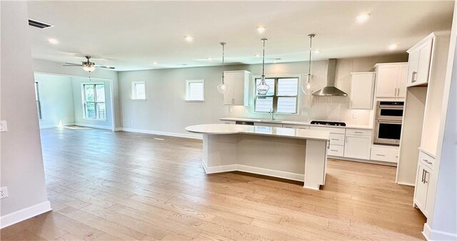 2808 Turnwater St, Hoschton, GA 30548 - kitchen featuring wall chimney range hood, stainless steel double oven, a kitchen island, black gas cooktop, and light wood finished floors