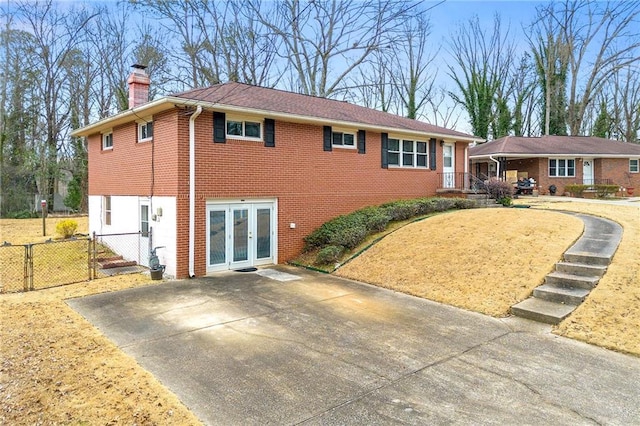 view of front of property featuring brick siding, fence, french doors, a gate, and a chimney