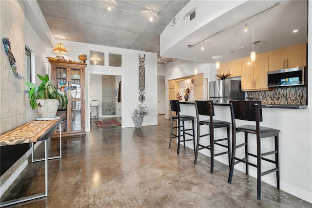 kitchen with pendant lighting, tasteful backsplash, a breakfast bar area, appliances with stainless steel finishes, and light brown cabinets