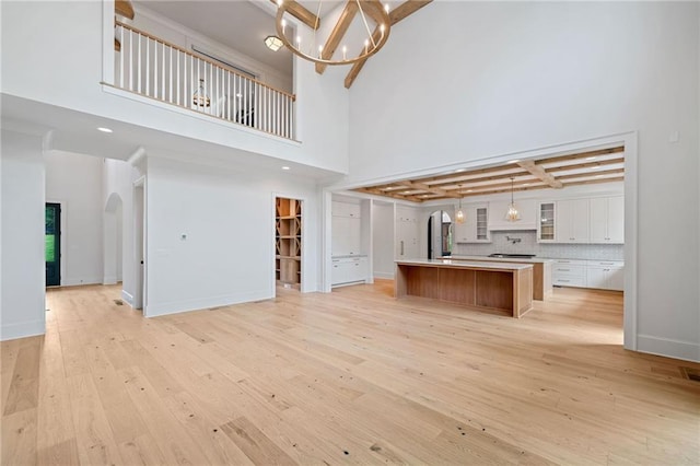 615 Claxton Ln, Milton, GA 30004 - unfurnished living room featuring a towering ceiling, light wood-style floors, a chandelier, arched walkways, and beamed ceiling