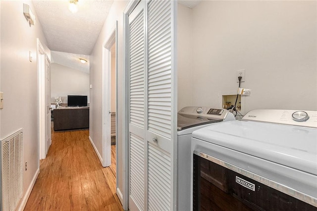 washroom featuring washing machine and dryer, light hardwood / wood-style floors, and a textured ceiling