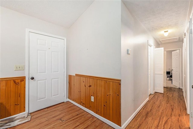 hallway with wood walls, light hardwood / wood-style floors, and a textured ceiling