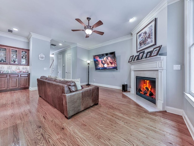 living area featuring ceiling fan, a glass covered fireplace, light wood finished floors, recessed lighting, and crown molding