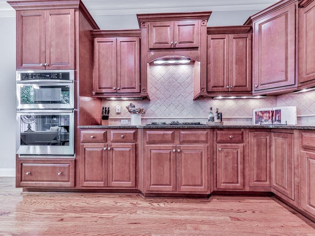 kitchen featuring stainless steel double oven, crown molding, dark stone countertops, backsplash, and gas cooktop